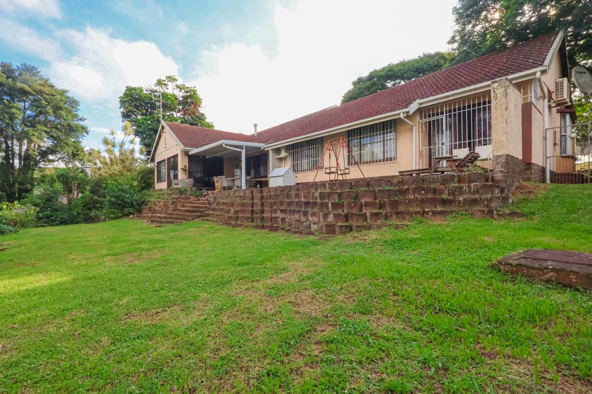 Rear view of the house featuring a large lawn, a raised stone retaining wall, and a covered patio area with security bars on windows.