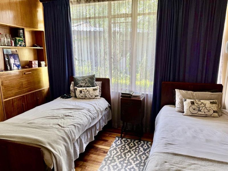 A bedroom featuring hardwood flooring, a large window with natural light, and a built-in wooden shelving unit.