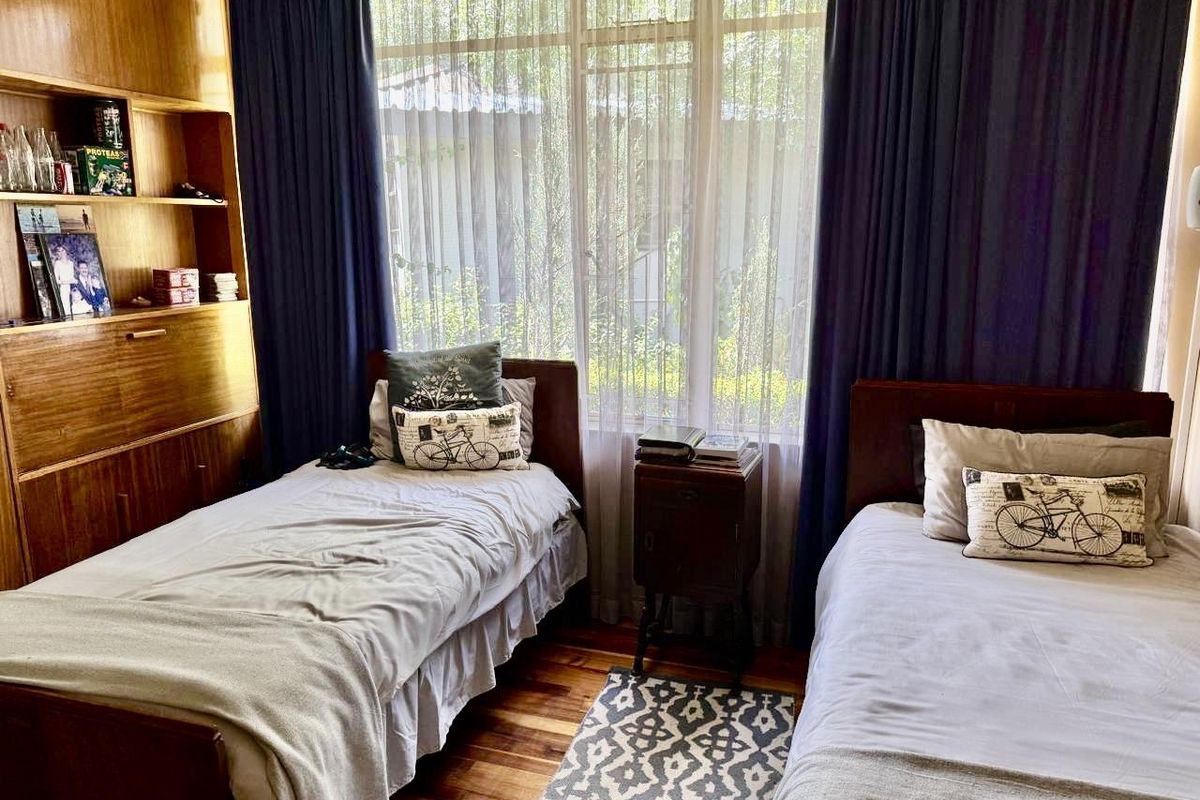 A bedroom featuring hardwood flooring, a large window with natural light, and a built-in wooden shelving unit.