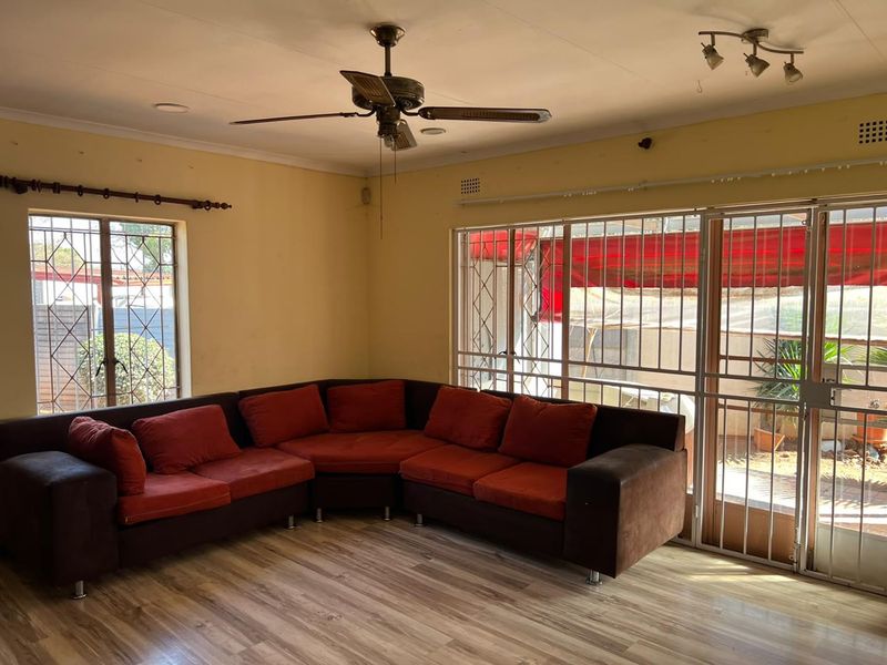Spacious living room featuring laminate flooring, a ceiling fan, and large windows with security bars, providing access to the outdoor area.