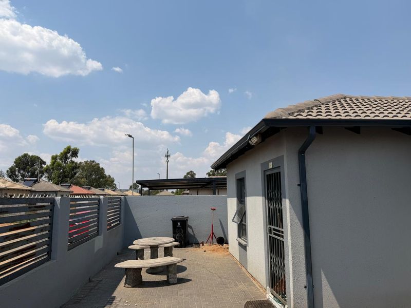 A paved rear patio area featuring a boundary wall, security gate, and tiled roof structure.