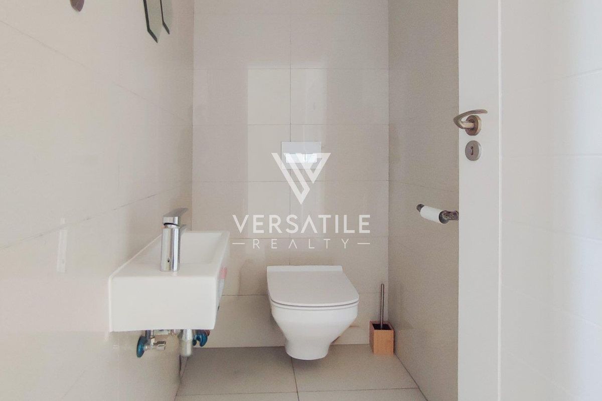 A clean, modern guest bathroom featuring a wall-mounted toilet and a compact wall-mounted basin with chrome fixtures.