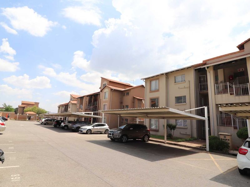 Exterior view of an apartment complex featuring covered parking bays and multi-story residential units with tiled roofing.