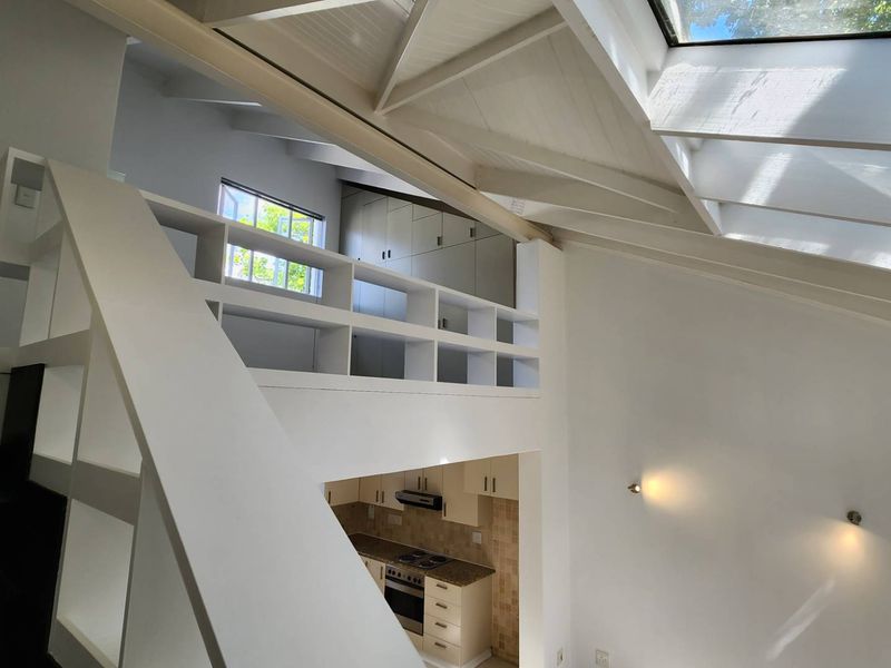 Bright open-plan living area featuring a mezzanine level, exposed timber rafters, skylights, and a functional kitchen with built-in cabinetry and appliances.