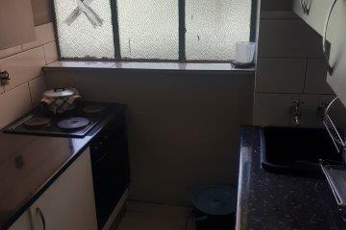 Compact kitchen featuring dark laminate countertops, built-in electric hob and oven, tiled flooring, and a window with a broken pane.