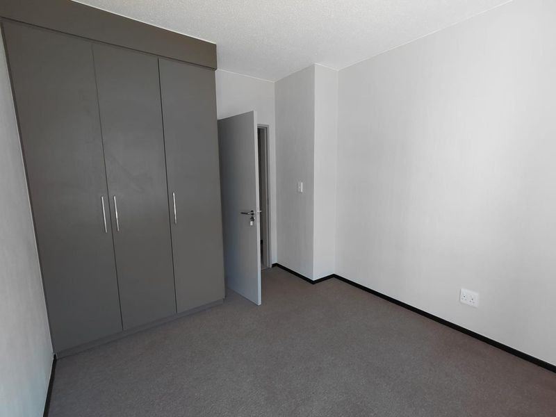 A clean, empty bedroom featuring neutral grey built-in cupboards, carpeted flooring, and a simple, modern aesthetic ready for personalization.