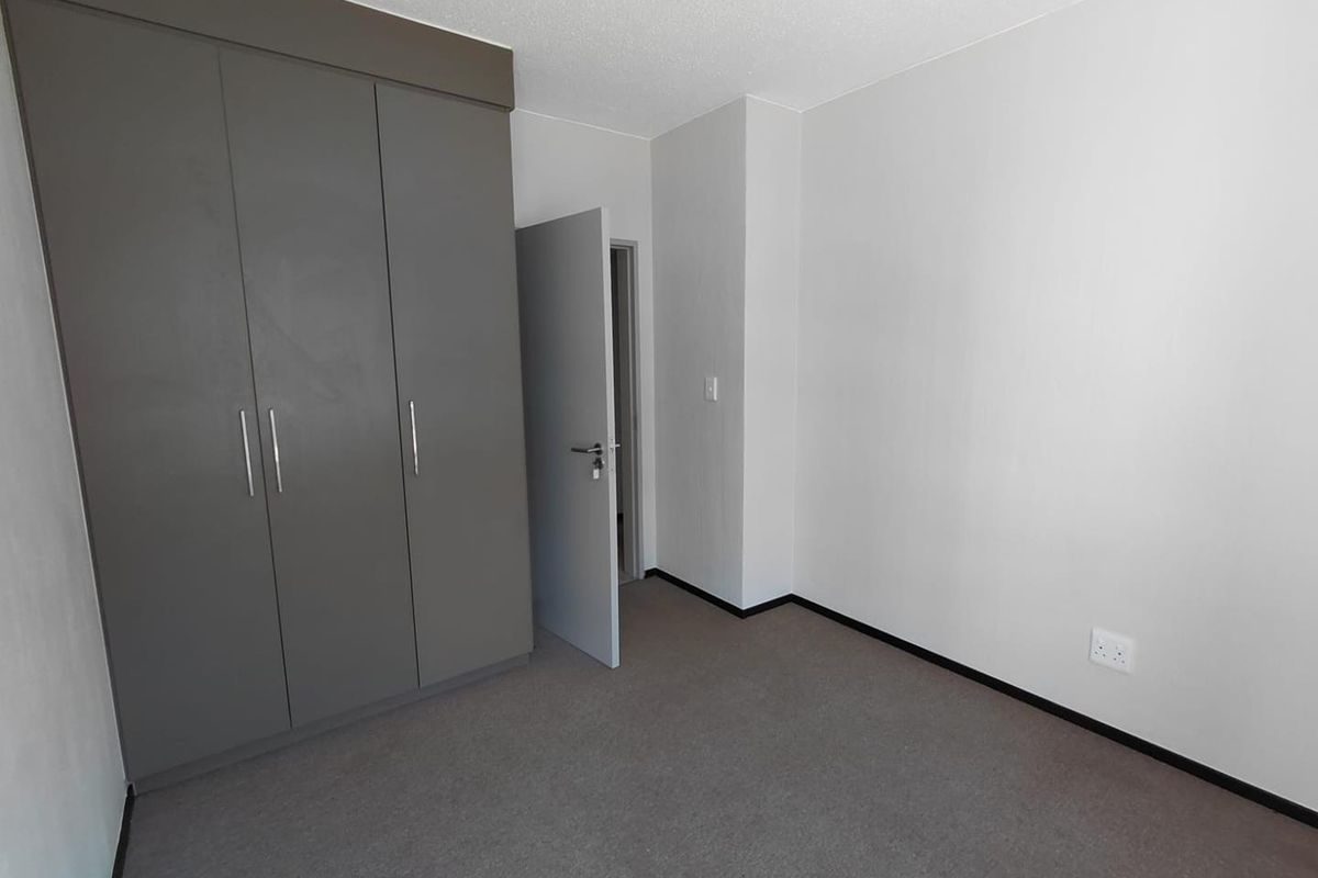 A clean, empty bedroom featuring neutral grey built-in cupboards, carpeted flooring, and a simple, modern aesthetic ready for personalization.