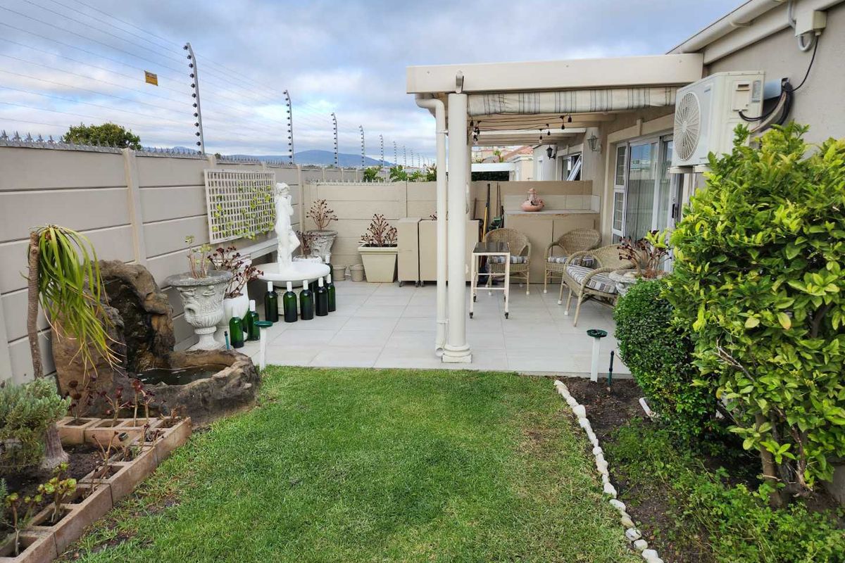 A private rear garden featuring a paved patio area with a covered pergola, a small water feature, and perimeter walling with electric fencing.