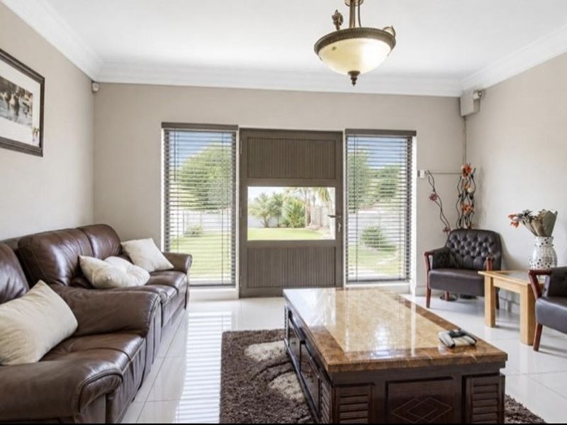 A well-maintained living room featuring tiled flooring, crown molding, and direct access to the garden through a central exterior door.