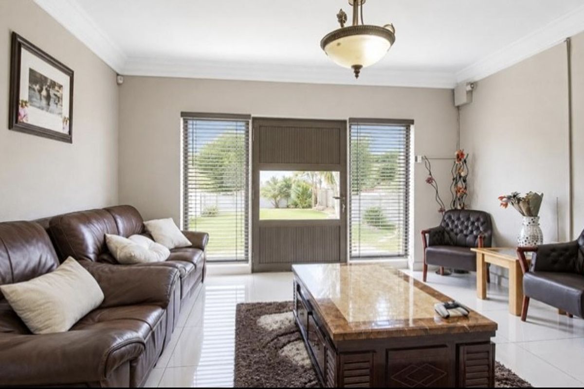 A well-maintained living room featuring tiled flooring, crown molding, and direct access to the garden through a central exterior door.