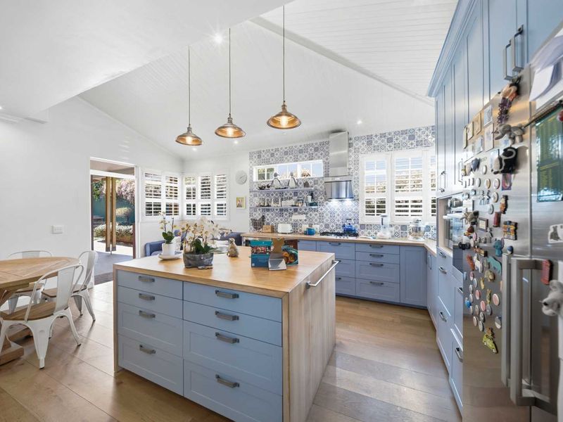 Spacious open-plan kitchen featuring a central island with timber countertop, shaker-style cabinetry, patterned tile backsplash, and vaulted ceilings with pendant lighting.