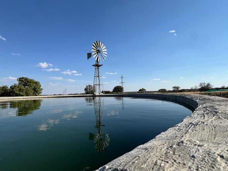 A large circular concrete water reservoir on a farm, featuring a traditional metal windmill in the background under a clear blue sky.