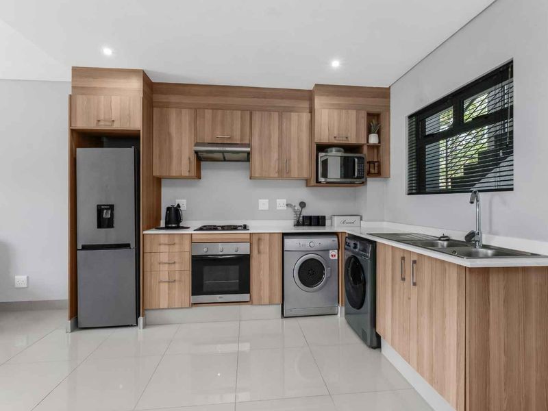 Modern kitchen featuring light wood cabinetry, stone countertops, integrated appliances, and sleek tiled flooring in a clean, well-maintained space.