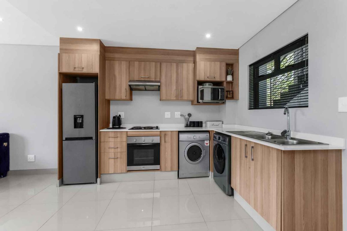 Modern kitchen featuring light wood cabinetry, stone countertops, integrated appliances, and sleek tiled flooring in a clean, well-maintained space.