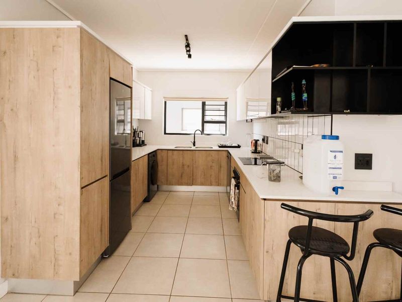 Modern galley-style kitchen featuring light wood-grain cabinetry, white countertops, integrated appliances, and tiled flooring in a clean, contemporary layout.
