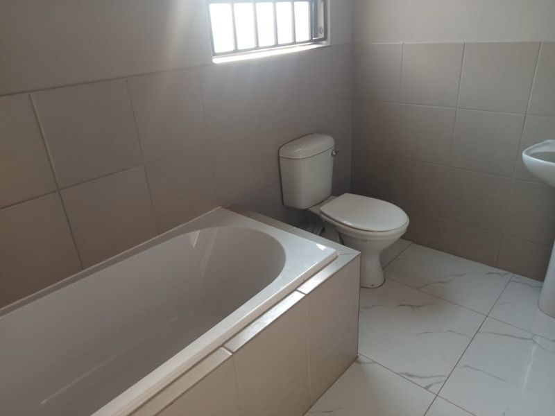 A clean, functional bathroom featuring a bathtub, toilet, and pedestal basin with neutral wall and floor tiling.