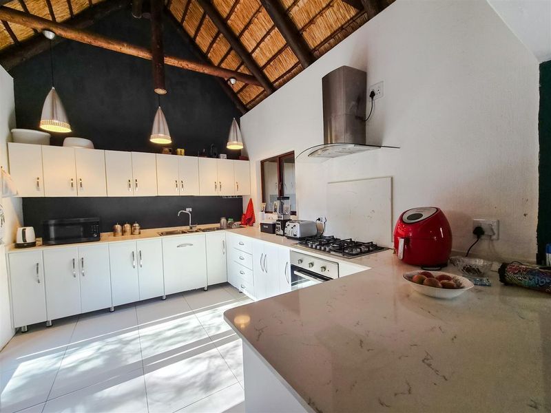 Modern kitchen featuring white cabinetry, stone countertops, gas hob, and a striking high-vaulted exposed thatch ceiling with pendant lighting.