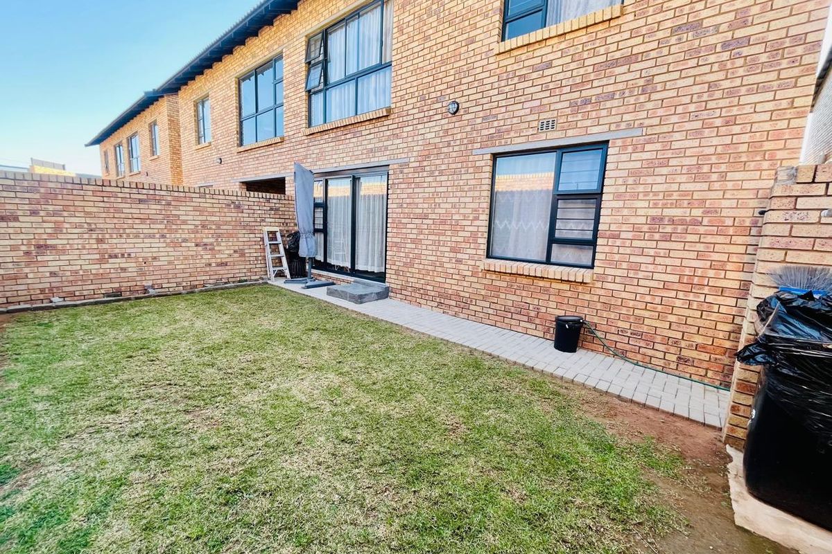 Rear view of a townhouse featuring a face brick facade, private garden with lawn, and a paved walkway leading to sliding glass doors.
