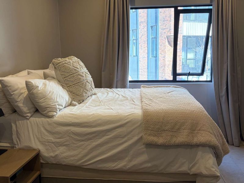 A well-lit bedroom featuring tiled flooring, neutral wall tones, and a large window with modern aluminium frames.
