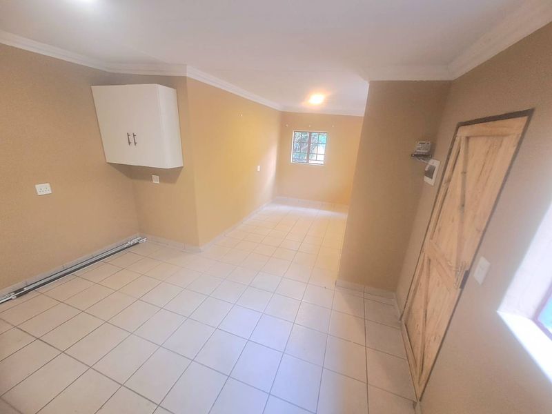 An empty, neutrally painted living area featuring tiled flooring, a wall-mounted storage cabinet, and a rustic timber door.