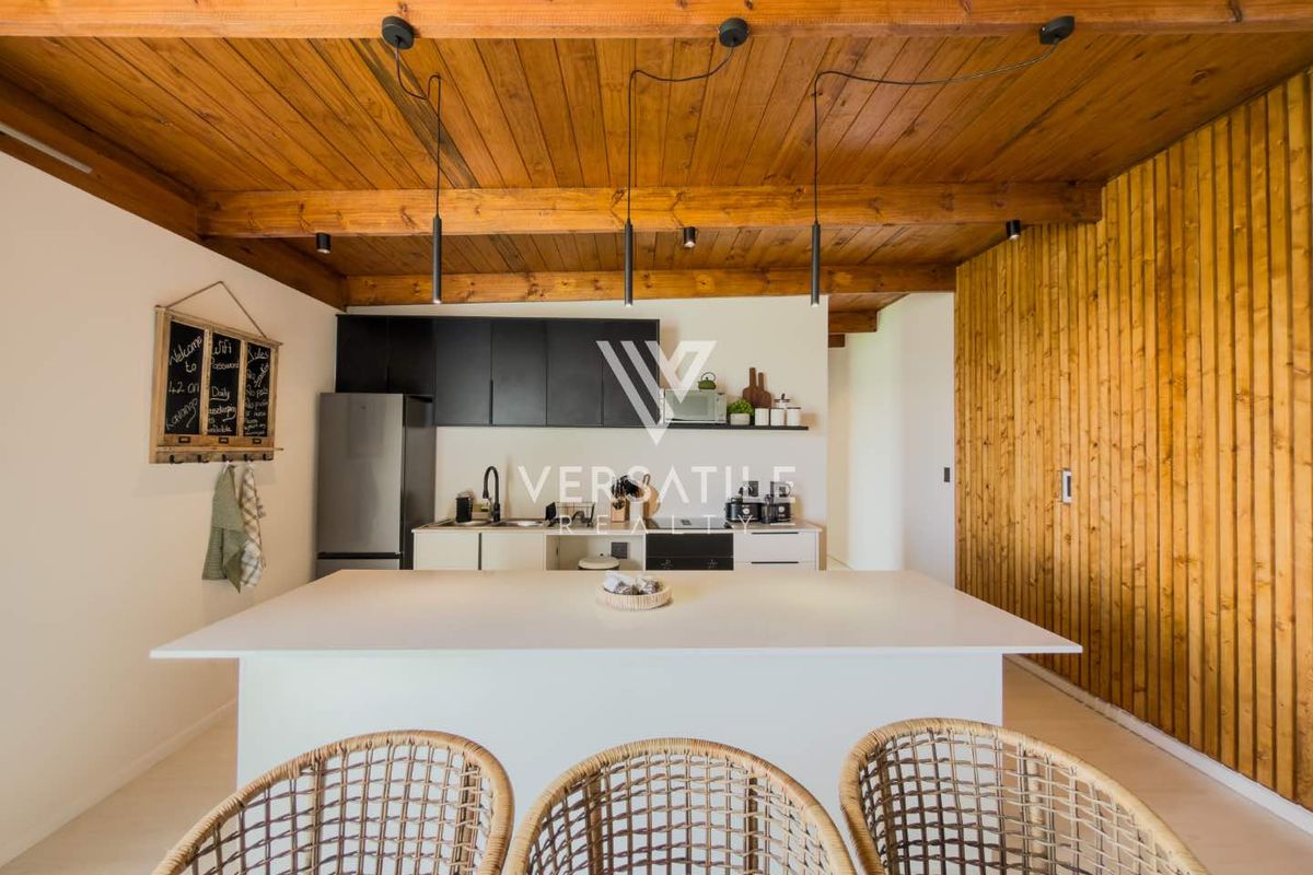 Modern kitchen featuring a central island, sleek cabinetry, and a distinctive exposed timber beam ceiling with integrated pendant lighting.
