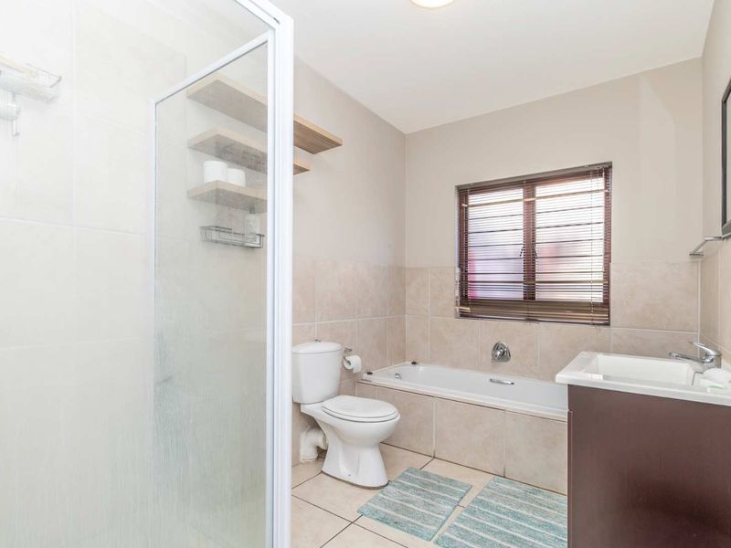 A well-maintained bathroom featuring a shower enclosure, bathtub, toilet, and a vanity cabinet with a basin, complemented by neutral wall and floor tiling.