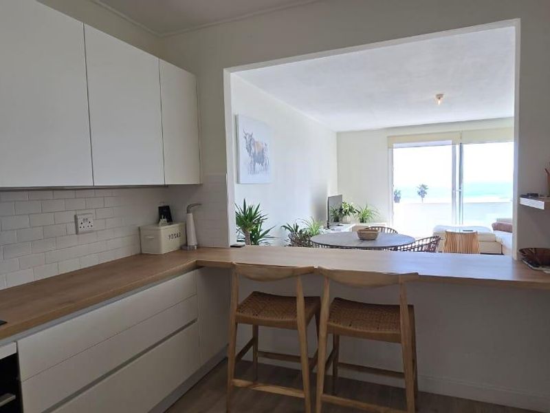 Modern open-plan kitchen featuring white cabinetry, wooden countertops, and a subway tile backsplash, seamlessly connecting to the living area with ocean views.