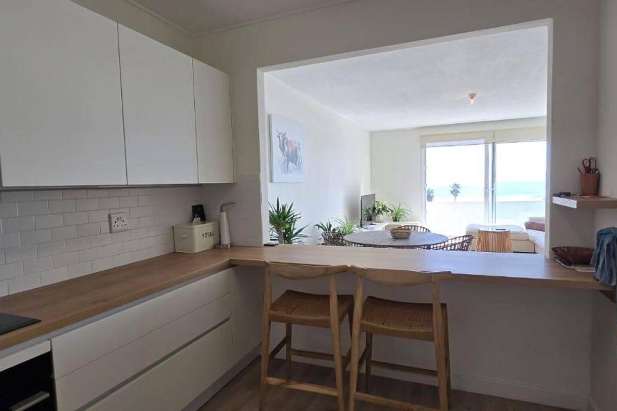 Modern open-plan kitchen featuring white cabinetry, wooden countertops, and a subway tile backsplash, seamlessly connecting to the living area with ocean views.