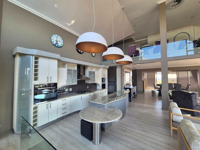 Spacious open-plan kitchen and living area featuring modern cabinetry, granite countertops, a central island, and a mezzanine level with glass balustrades.