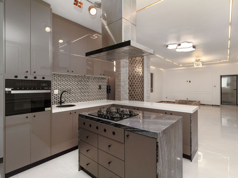Modern open-plan kitchen featuring high-gloss cabinetry, stone island with integrated gas cooktop, and premium finishes, seamlessly flowing into the spacious living area.