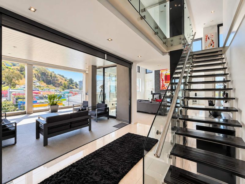 Modern open-plan living area featuring a striking glass-railed staircase, seamless indoor-outdoor flow to a covered balcony, and high-quality finishes throughout.