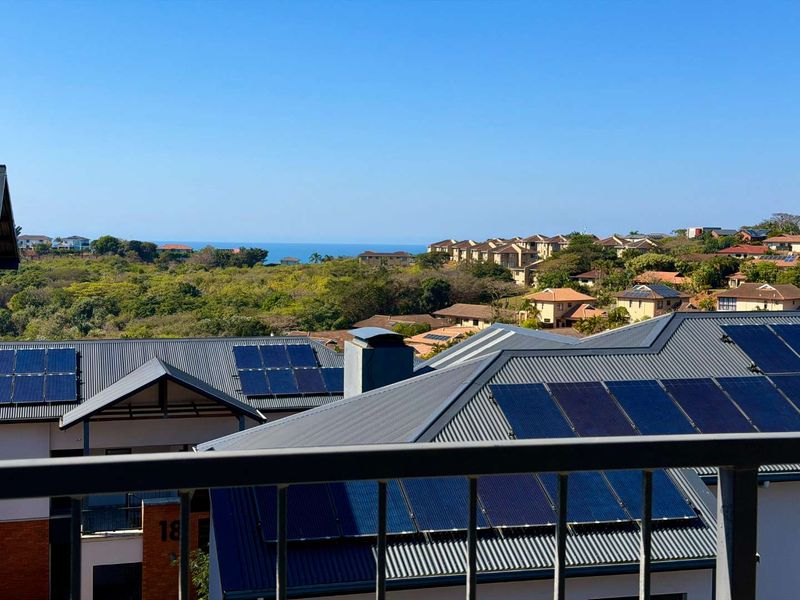 Elevated view overlooking a residential estate with solar-equipped metal roofs and a distant ocean horizon.