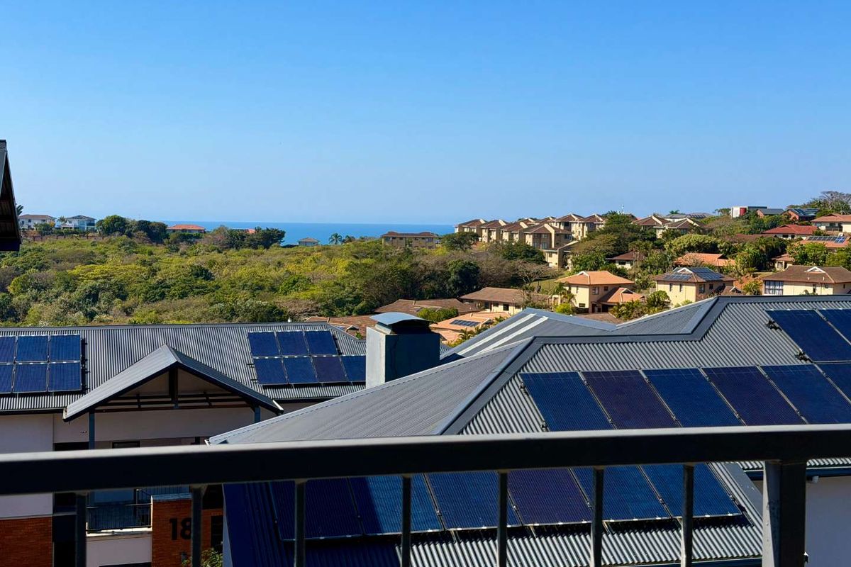 Elevated view overlooking a residential estate with solar-equipped metal roofs and a distant ocean horizon.