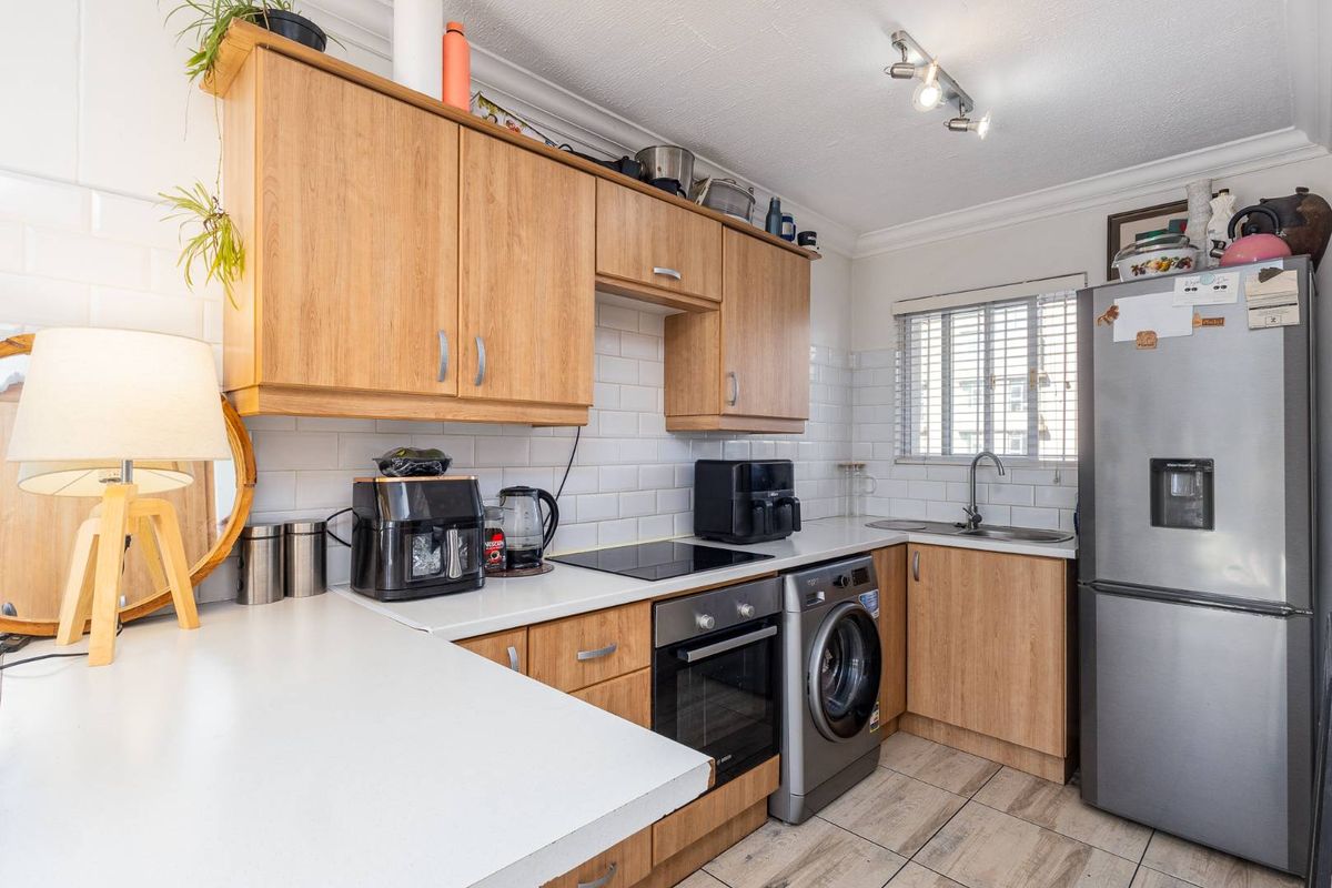 A functional kitchen featuring light wood cabinetry, subway tile backsplash, integrated oven and hob, and tiled flooring with ample counter space.