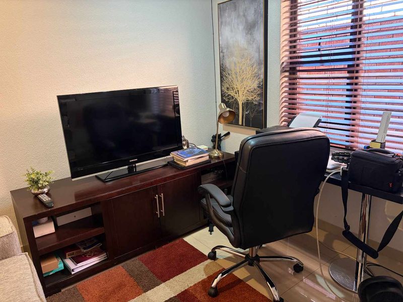 A functional home office space featuring tiled flooring and adjustable venetian blinds, providing a practical area for work or study.