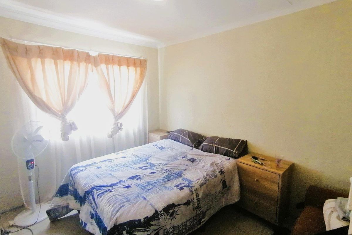 A standard bedroom featuring tiled flooring, neutral wall finishes, and a window with fitted curtain rails.