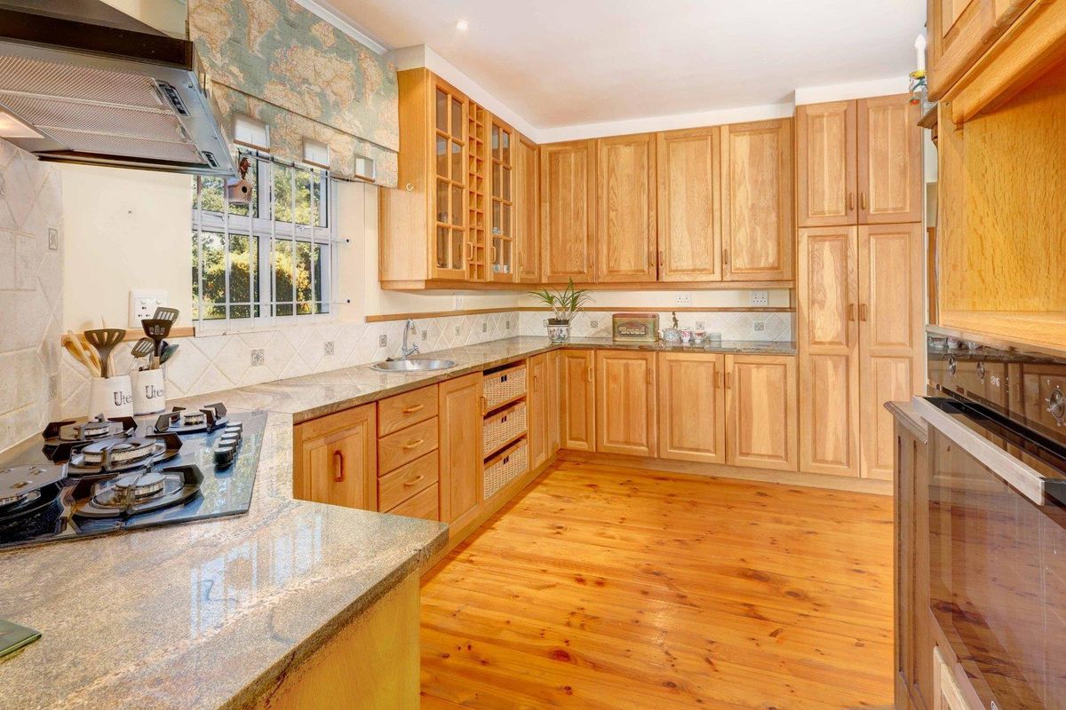 A functional kitchen featuring warm timber cabinetry, granite countertops, a gas hob, and built-in oven, complemented by natural timber flooring.
