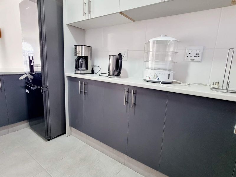 Modern kitchen featuring dark grey cabinetry, white stone countertops, and tiled flooring, offering a clean and functional workspace.