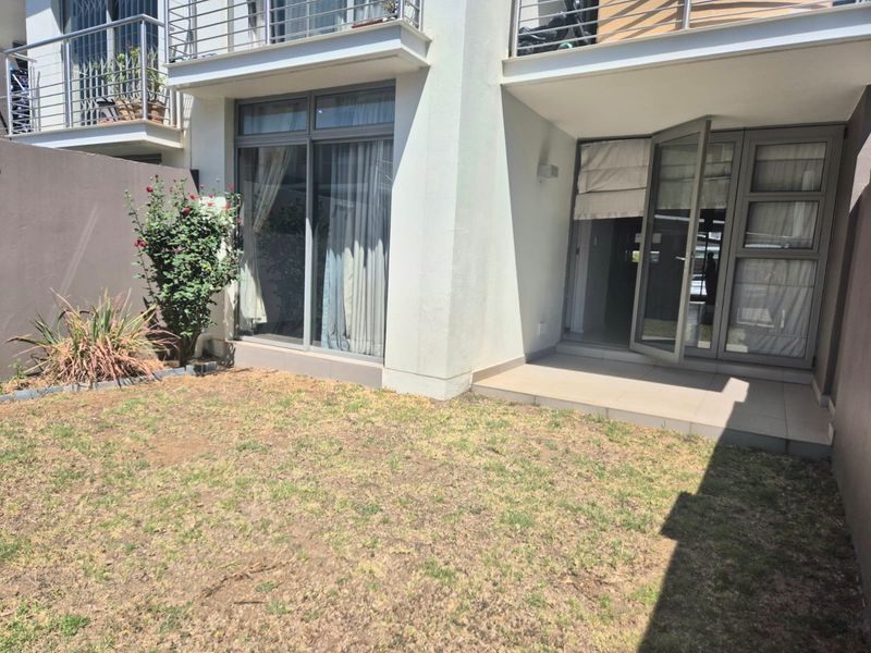 Rear view of the apartment featuring a private garden, tiled patio area, and direct access through sliding glass doors to the living space.