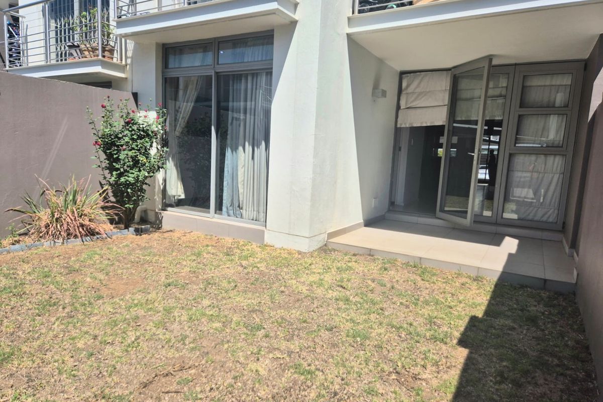 Rear view of the apartment featuring a private garden, tiled patio area, and direct access through sliding glass doors to the living space.