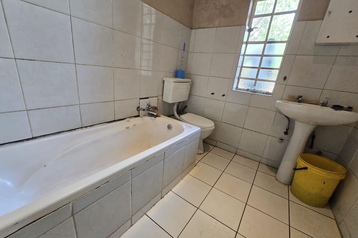 A dated bathroom featuring a standard bathtub, pedestal basin, and toilet with tiled walls and flooring, requiring significant renovation and cosmetic updates.