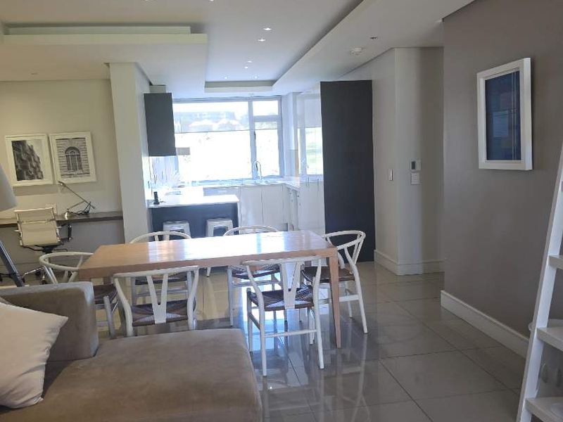 Modern open-plan living and dining area featuring sleek porcelain tiles, recessed ceiling lighting, and a contemporary kitchen with a central island.