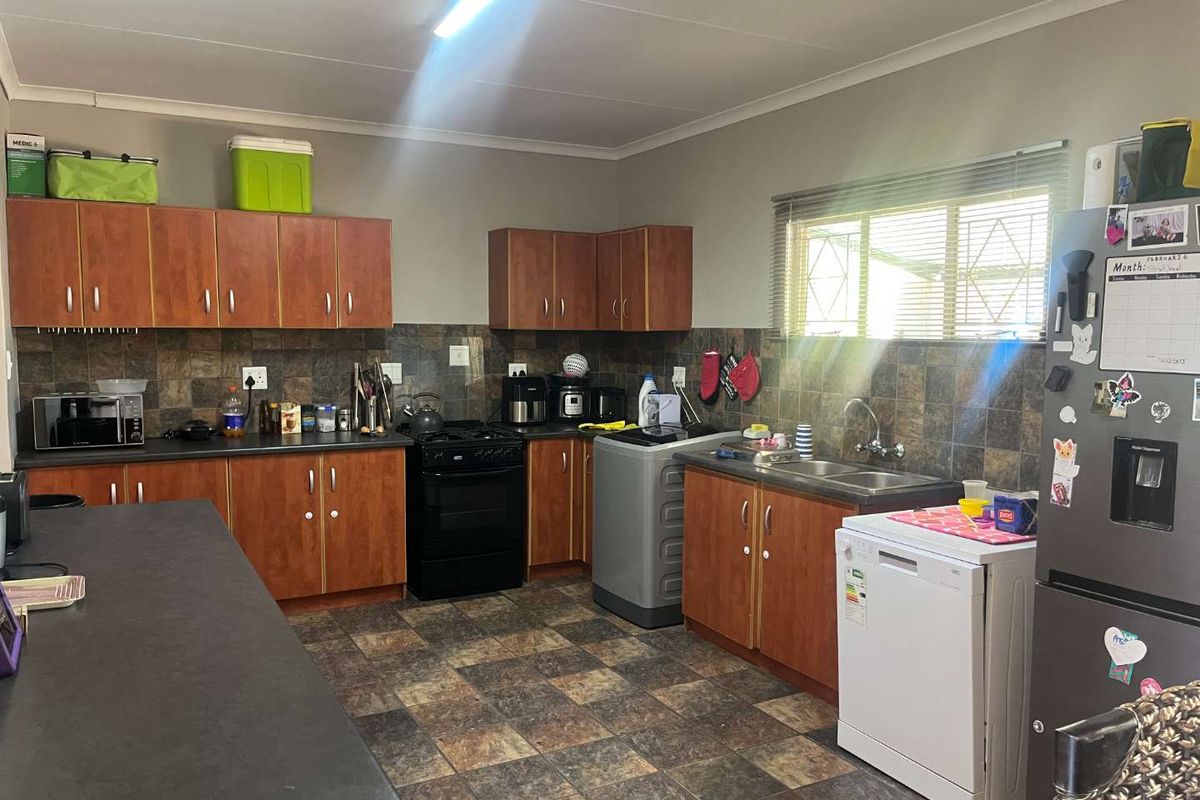 Functional kitchen featuring wood-finish cabinetry, dark laminate countertops, tiled splashback, and integrated sink with window view.