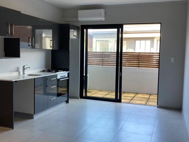 Modern open-plan kitchen featuring sleek dark cabinetry, stone countertops, and built-in appliances, leading directly to a private balcony through sliding glass doors.