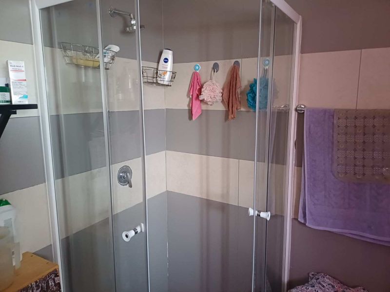 A functional bathroom shower enclosure featuring a glass door, chrome shower fixtures, and horizontal striped wall tiling.
