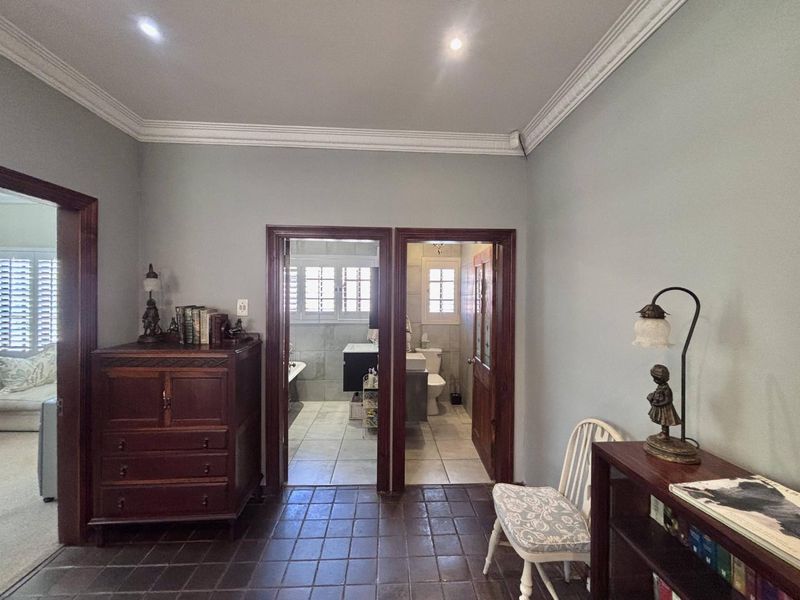 A well-maintained hallway featuring classic crown molding, dark tiled flooring, and wooden door frames leading into adjacent rooms.