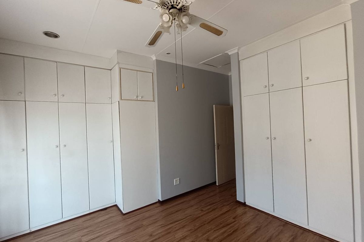 A bedroom featuring extensive built-in cabinetry, wood-look laminate flooring, and a ceiling fan, offering ample storage space.