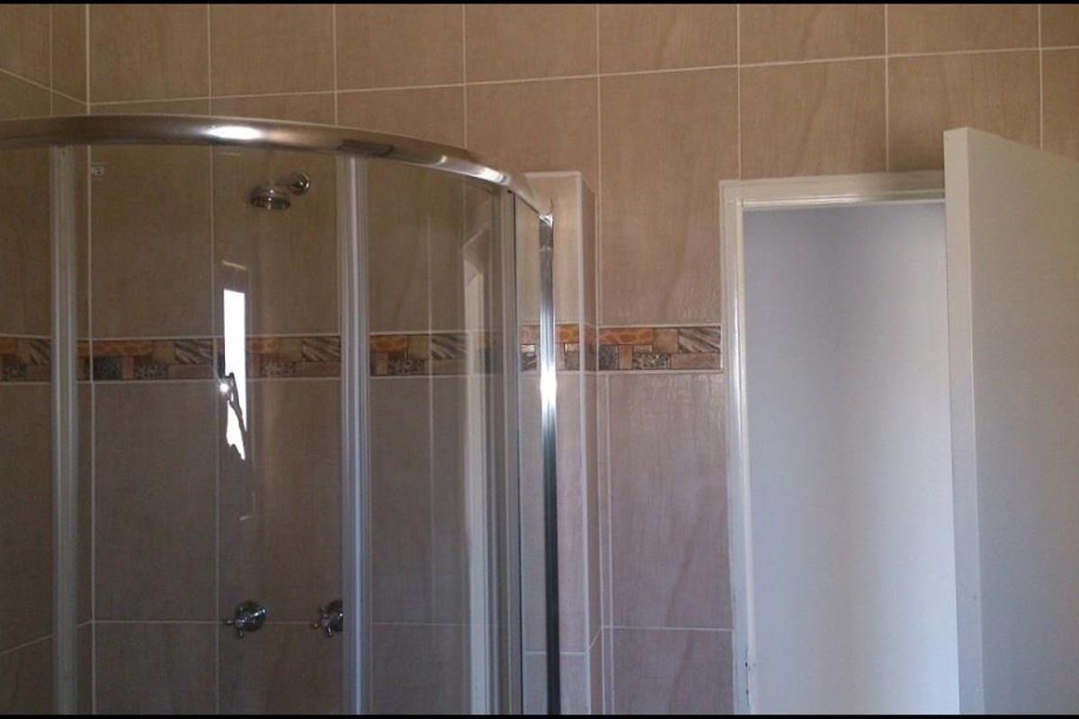 A functional bathroom featuring a curved glass shower enclosure with tiled walls and a decorative border.
