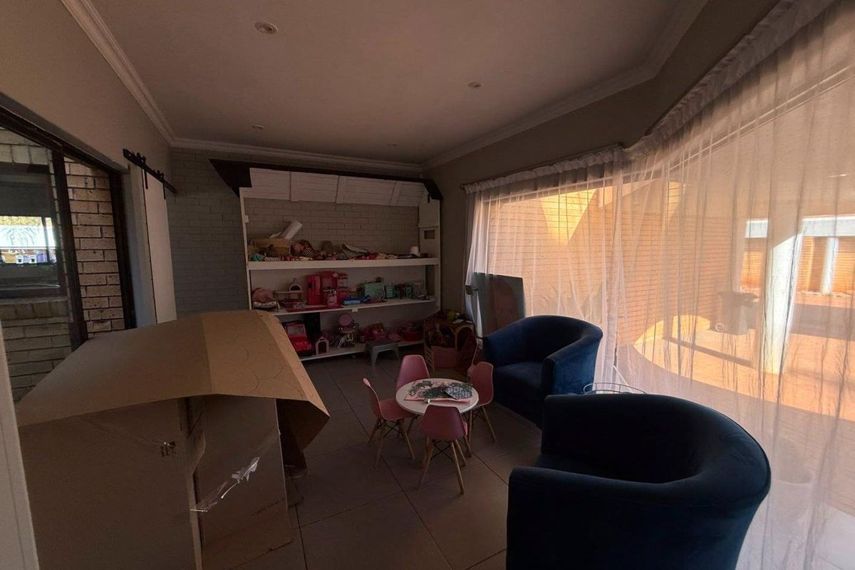 A living area featuring tiled flooring, built-in shelving, and large windows with sheer curtains, providing access to an outdoor patio space.