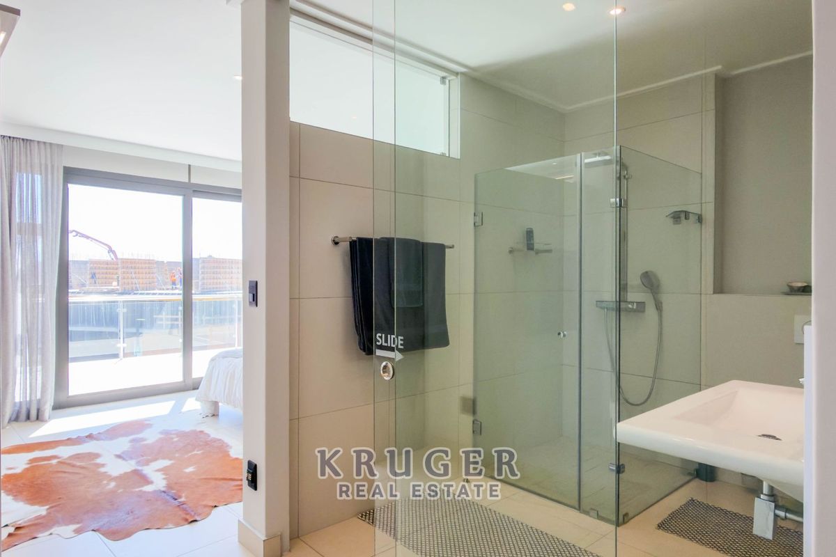 Modern en-suite bathroom featuring a glass-enclosed shower, wall-mounted basin, and sleek contemporary finishes, seamlessly integrated with the adjacent bedroom area.